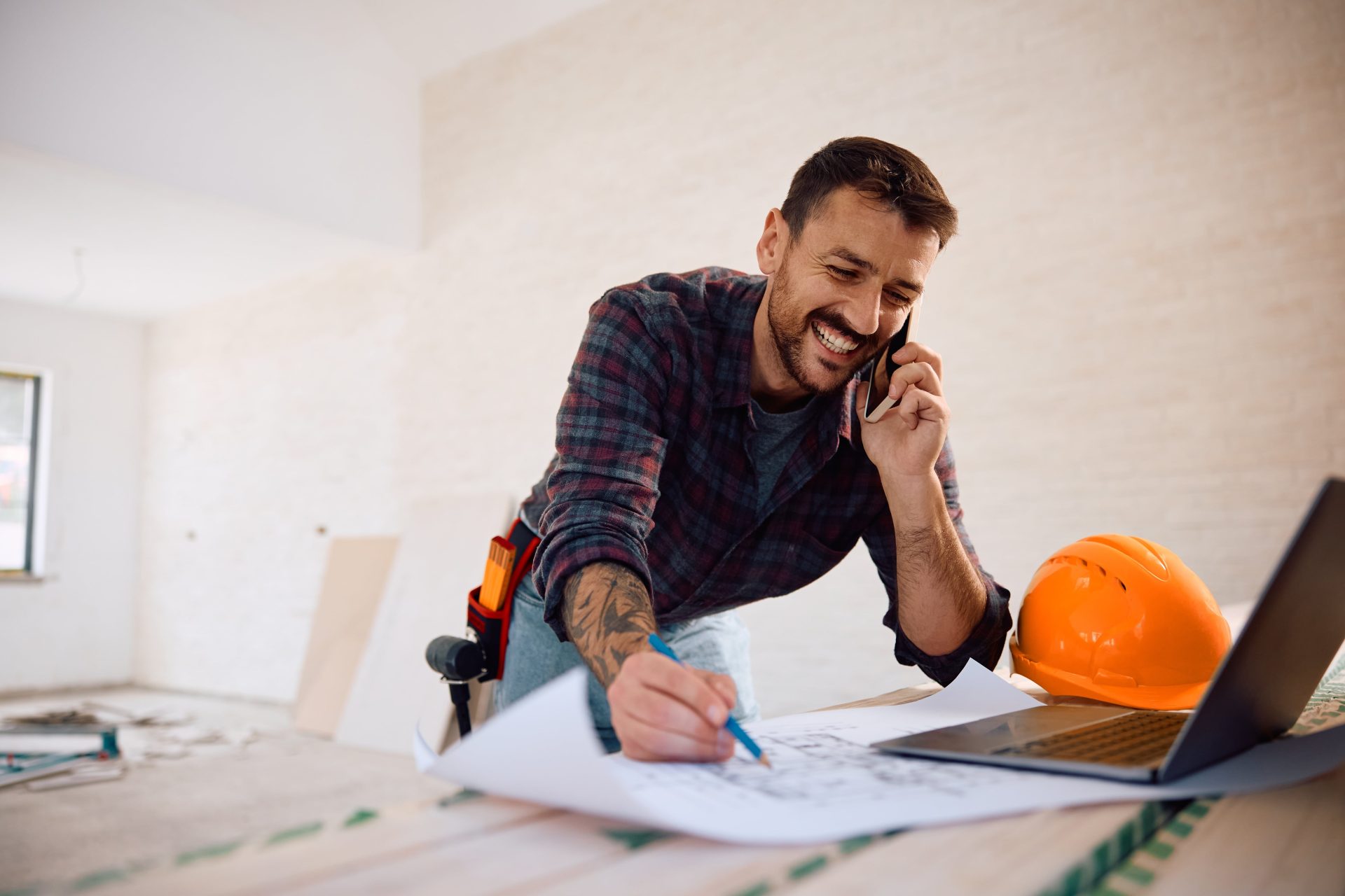 Construction manager discussing home plans on phone while reviewing blueprints.